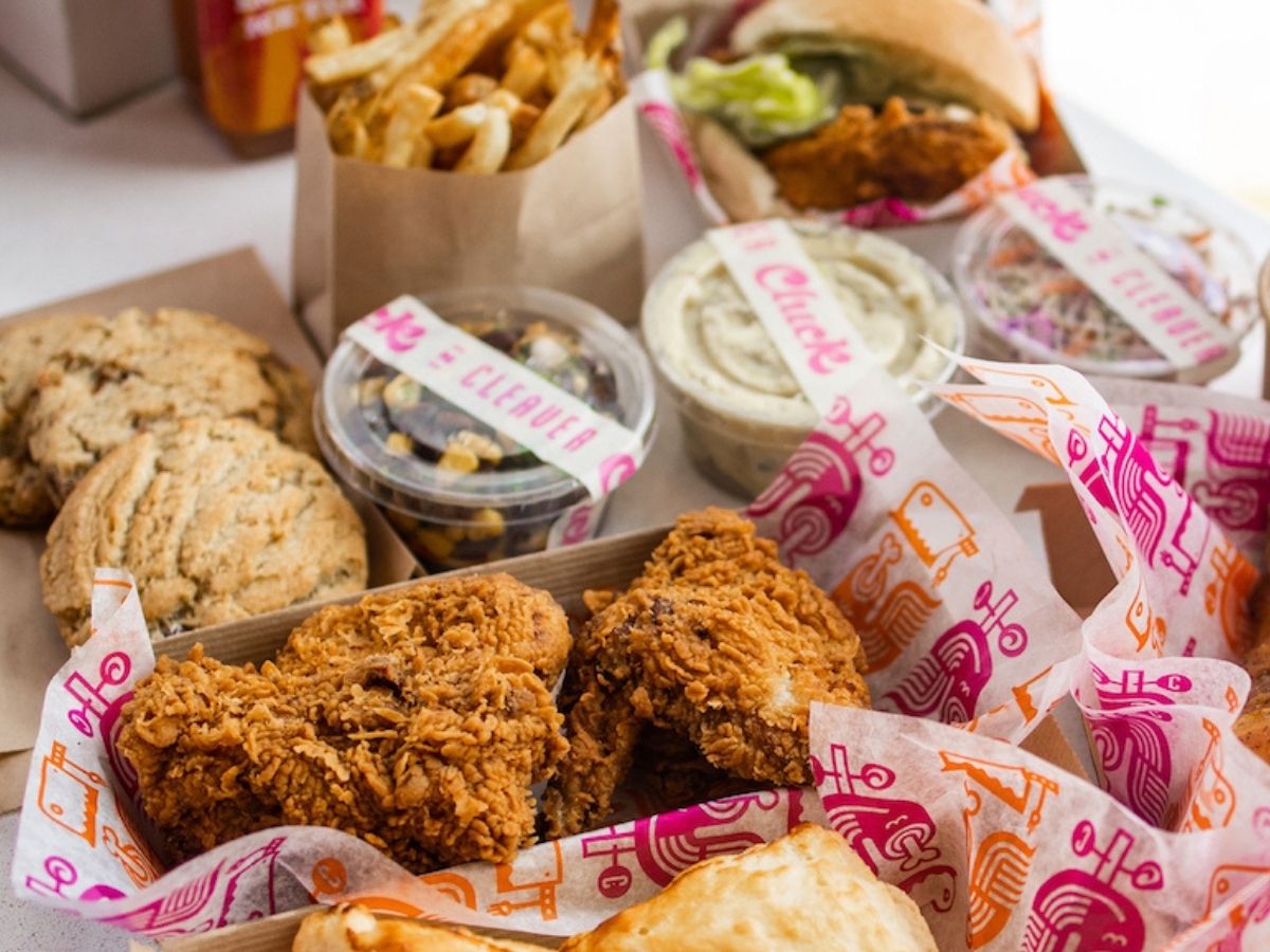 Fried chicken pieces with crispy coating, fresh-baked buttermilk biscuits, cookies, sides including coleslaw and corn salad, and golden fries in takeout packaging from Cluck N Cleaver.