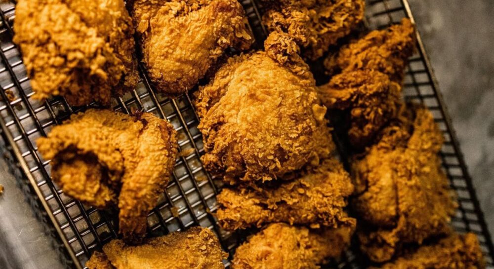 Fried chicken pieces on a cooling rack, showcasing Cluck N Cleaver's chef-crafted, crispy fried chicken, emphasizing quality and local sourcing.