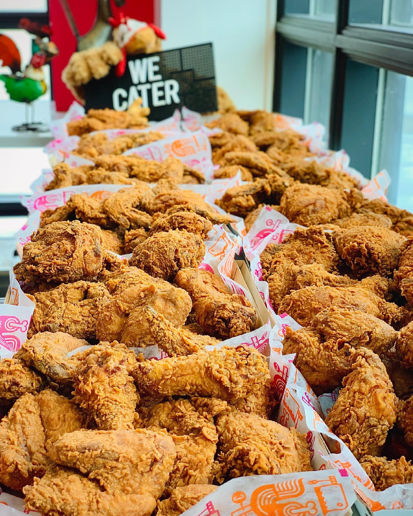 Catering display of Cluck N Cleaver's halal fried chicken, featuring a variety of crispy chicken pieces in serving baskets with branded paper, emphasizing quality comfort food for events and gatherings.